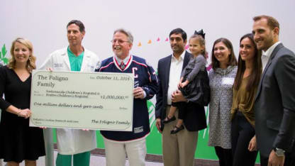 Photo of Boone Jenner and family posing with a group of representatives from Nationwide Children's Hospital. They are holding a large check given to Nationwide Children's from the Foligno family for one million dollars.