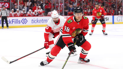 Connor Bedard #98 of the Chicago Blackhawks controls the puck against Joe Veleno #90 of the Detroit Red Wings