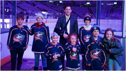 Photo of Blue Jackets alternate captain, Zach Werenski, posing with a group of pediatric cancer heroes in front of the ice.