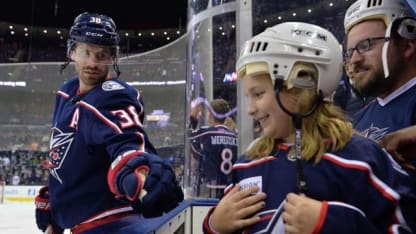 Photo of Boone Jenner reaching out to fist bump a young Blue Jackets fan standing on the team bench during warmups at a Blue Jackets game.