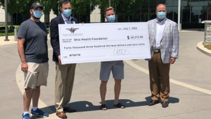 Photo of Cam Atkinson posing for a photo with representatives from the Ohio Health Foundation. They are holding a large check given to the Ohio Health Foundation for forty thousand three hundred and thirteen dollars.