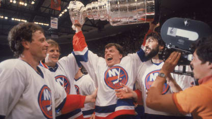 Swedish ice hockey player Anders Kallur (center) of the New York Islanders raises the Stanley Cup aloft as he celebrates victory with teammates, from left, Canadian Wayne Merrick, Swede Stefan Persson, and Canadian John Tonelli, while a cameraman goes in for a close-up, Uniondale, New York, May 21, 1981. (Photo by Bruce Bennett Studios via Getty Images Studios/Getty Images)