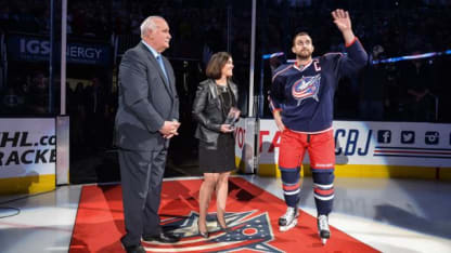 Photo of Nick Foligno waving to the crowd at Nationwide Arena with President of Hockey Operations, John Davidson, and Senior Vice President and Chief Marketing Officer Kathryn Dobbs.