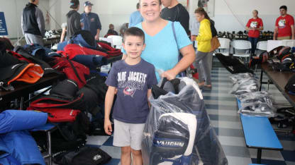 Photo of a woman and a young boy smiling while holding a bag of hockey equipment at the Blue Jackets Equipment Sale.