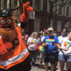 Gritty waves rainbow flag while marching in Philly Pride Parade