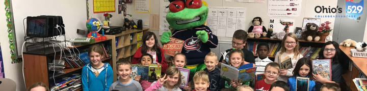 Photo of Blue Jackets mascot, Stinger, posing with a classroom of young students. Everyone is holding a book.