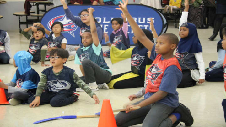 Photo of a group of young kids raising their hands to answer a question at a Hockey To Go clinic.