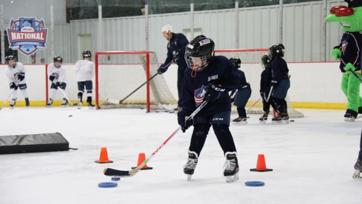 Photo of young child stick handling with a puck in Blue Jackets hockey gear on the ice during a Learn To Play clinic.