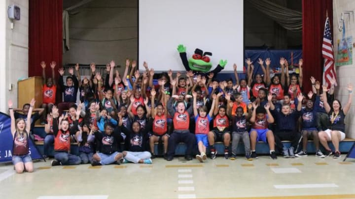 Photo of Blue Jackets mascot, Stinger, posing with a group of young kids at a Hockey To Go clinic cheering with their hands in the air.