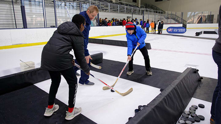 Photo of two students learning how to engage in a hockey face off from a Blue Jackets volunteer coach.