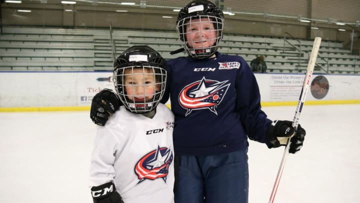 Photo of two young children in Blue Jackets hockey gear on the ice posing for a photo during a Learn To Play clinic.