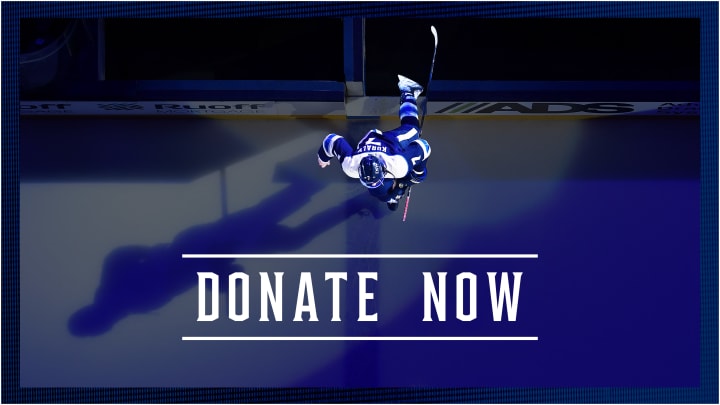 Graphic with blue border showing an aerial shot of Blue Jackets player, Sean Kuraly, entering the ice at Nationwide Arena with a dark blue overlay. White text below reads Donate Now.