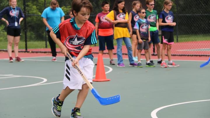 Photo of a young boy running with a hockey stick at a street hockey rink during a Hockey To Go clinic.