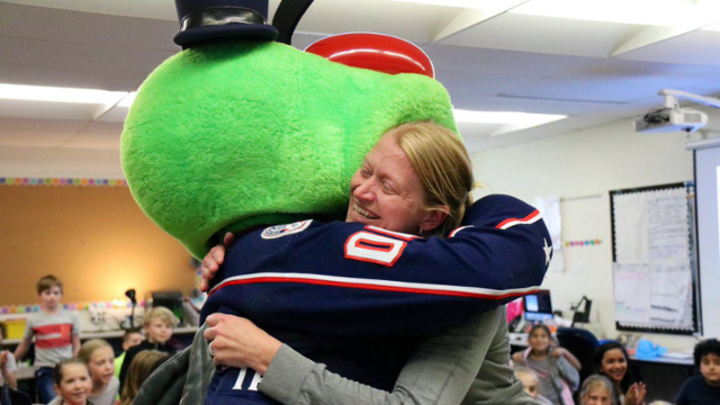 Photo of Blue Jackets mascot, Stinger, hugging a teacher in their classroom.