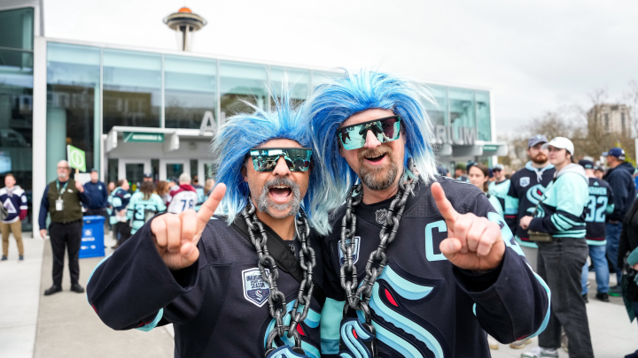 photo of two men wearing buoy wigs and dark blue kraken jerseys posing outside of climate pledge arena