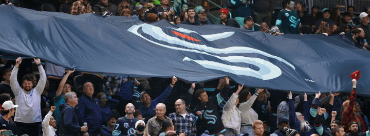 seattle kraken fans in the stands with a navy blue kraken flag hovering above them