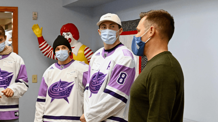 Photo of Blue Jackets players, Zach Werenski and Nick Blankeburg, speaking with a representative of the Ronald McDonald house during a team visit.
