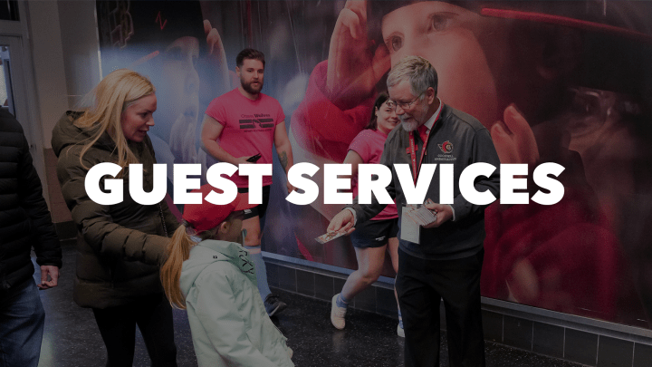 Photo of a Canadian Tire Centre staff member handing a young fan a pack of hockey cards with the words "Guest Services" in white letters.